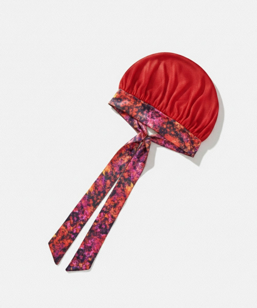 Flat lay of a Lew's Collections satin hair bonnet, featuring a vibrant red mesh lattice cap and a multicolored 'Cloudy Blossom' adjustable satin tie band with a knot.