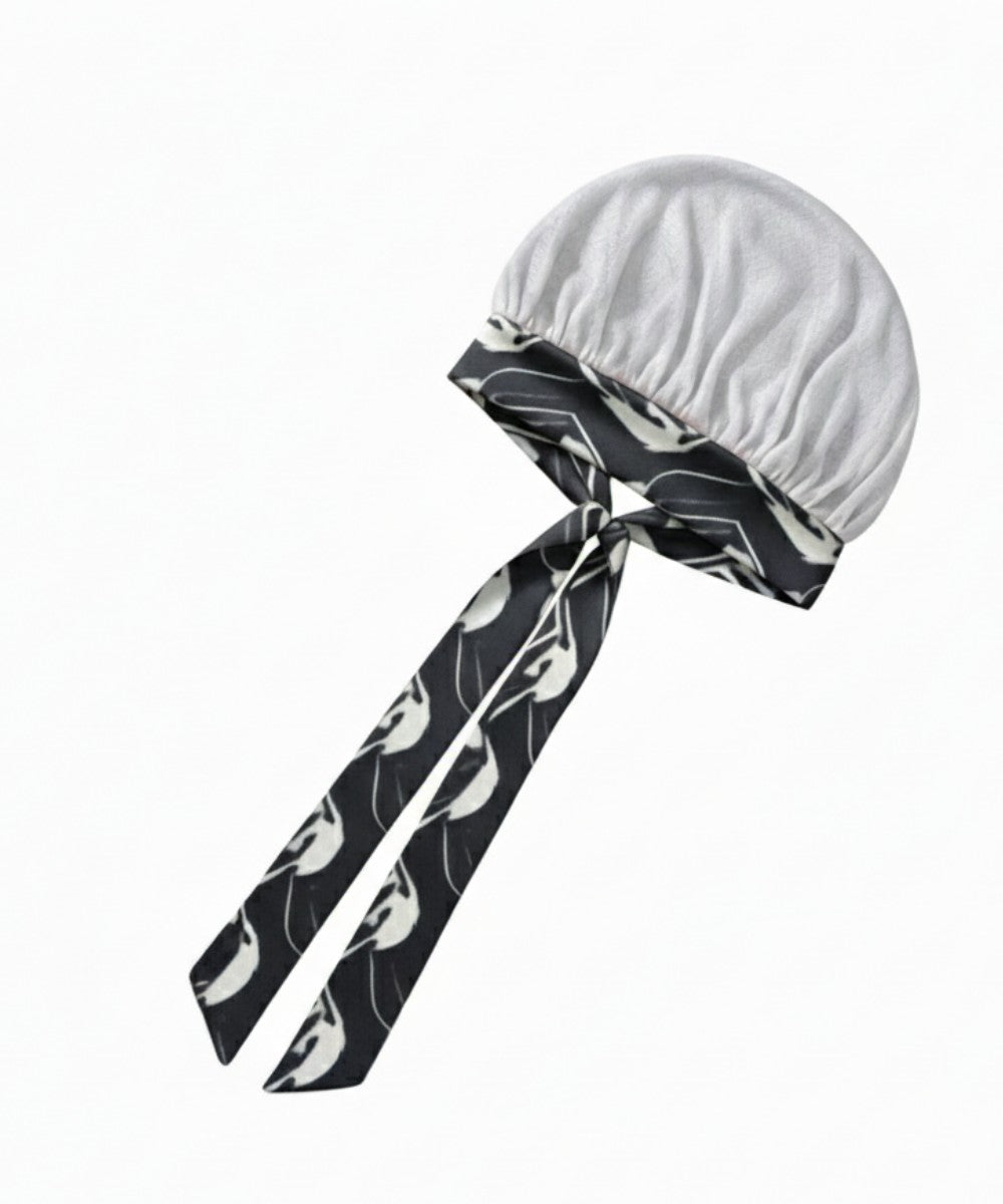 Flat lay of a Lew's Collections satin hair bonnet, featuring a cool white mesh lattice cap and a multicolored 'Marble Noir' adjustable satin tie band with a knot.