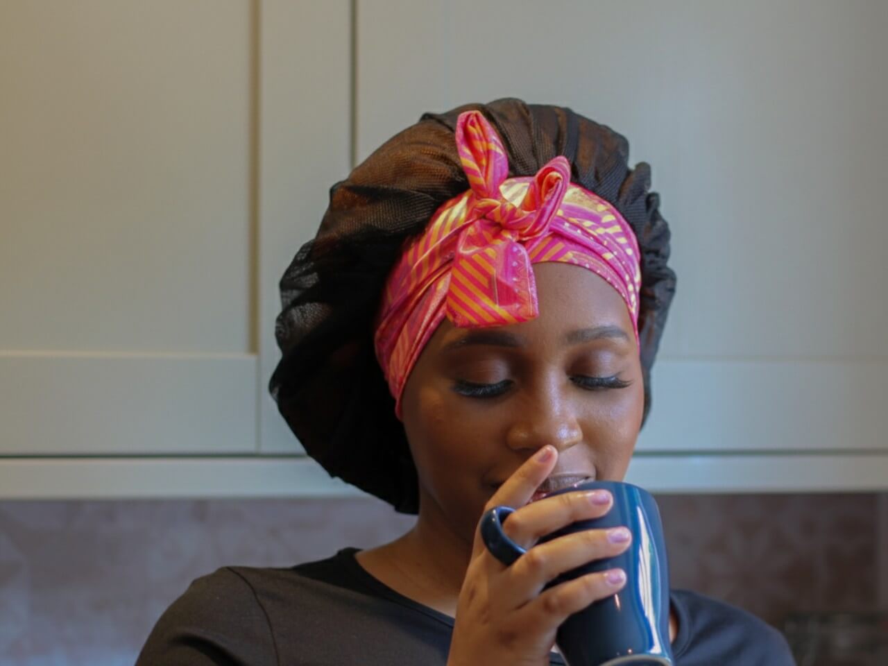 woman in a kitchen wearing a lews collections adjustable tie satin hair bonnet with black mesh and aztec afrique design 