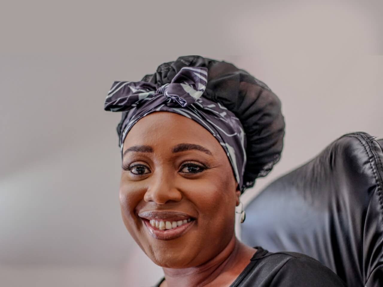 woman sitting on an office chair with a lew's collections satin hair bonnet in the adjustable tie band and marble noir design