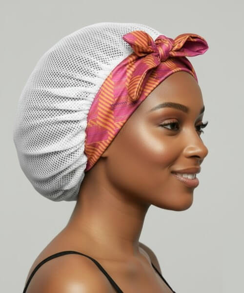 Profile shot of a smiling woman wearing a white breathable satin hair bonnet with a tied, vibrant pink and orange patterned satin band, highlighting hair protection.